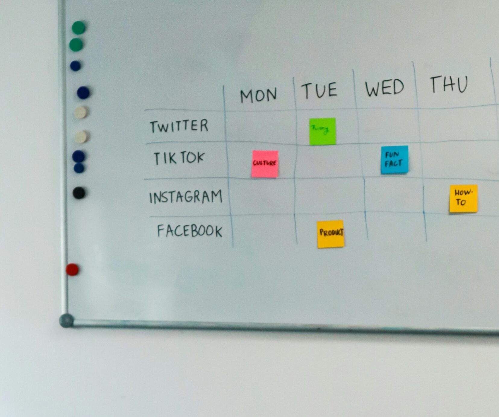 A modern office setup featuring a laptop and a whiteboard schedule for social media platforms.
